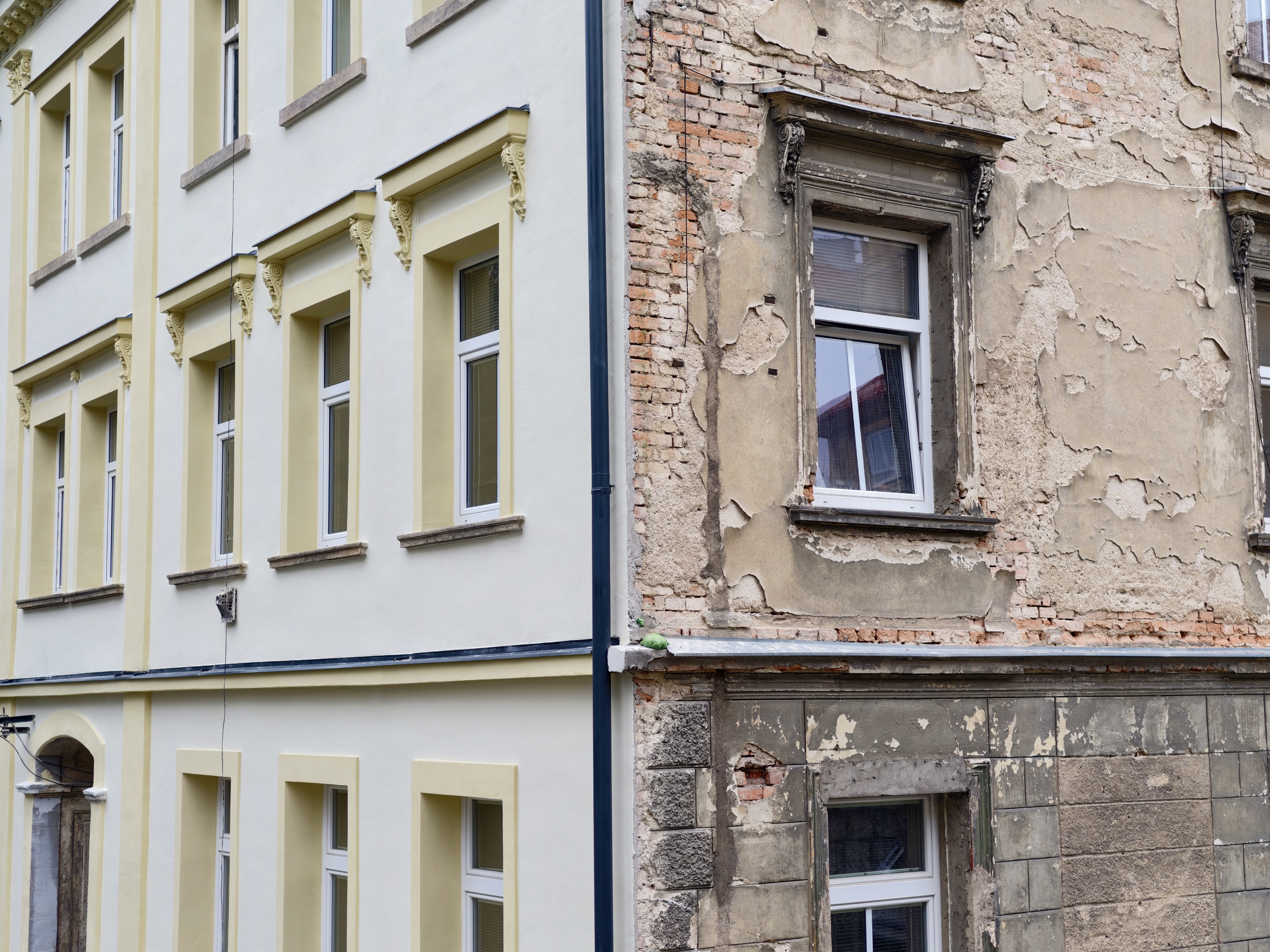 Half renovated building contrasting decay, bright yellow plaster meeting exposed brick and crumbling render,